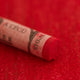 A close-up of a red Sennelier extra soft pastel. on the same coloured background, with the colour information printed on the paper wrap.