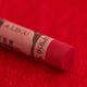 A close-up of a red Sennelier extra soft pastel on the same coloured background, with the colour information printed on the paper wrap.