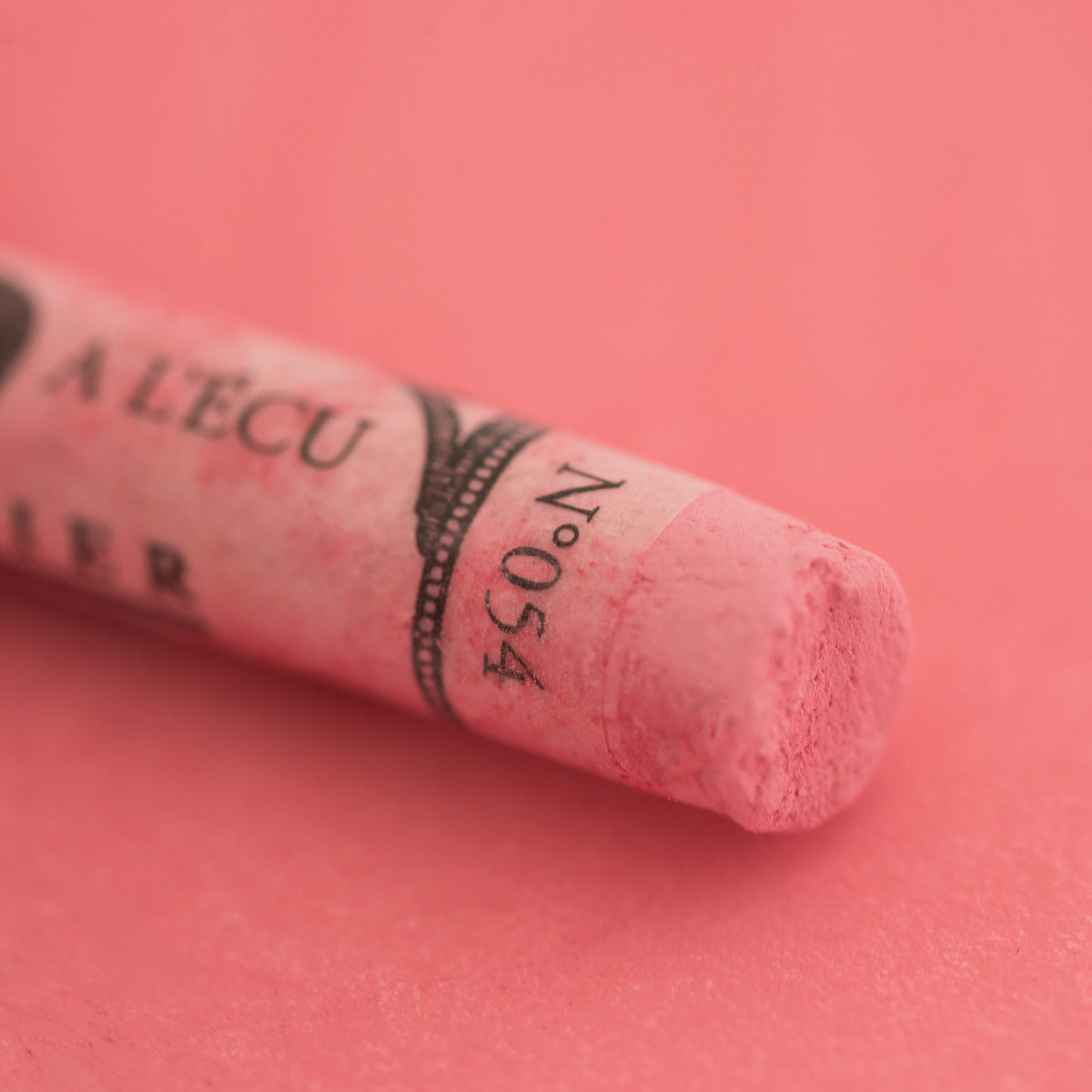 A close-up of a soft red Sennelier extra soft pastel on the same coloured background, with the colour information printed on the paper wrap.