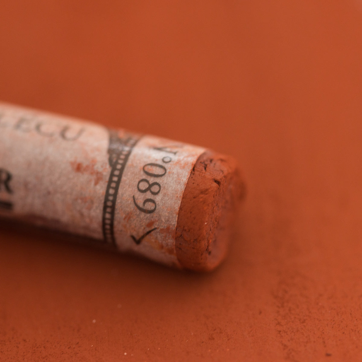 A close-up of a brown Sennelier extra soft pastel with the colour information printed on the paper wrap.