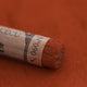 A close-up of a brown Sennelier extra soft pastel with the colour information printed on the paper wrap.