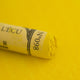 A close-up of a yellow Sennelier extra soft pastel. on the same coloured background, with the colour information printed on the paper wrap.