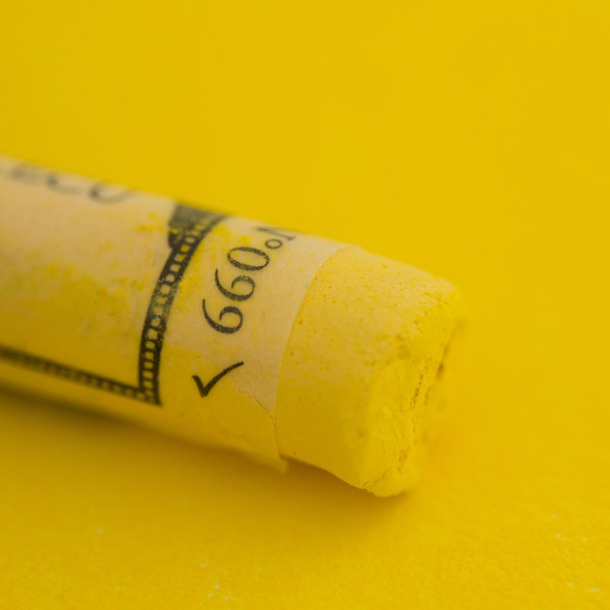 A close-up of a yellow Sennelier extra soft pastel. on the same coloured background, with the colour information printed on the paper wrap.