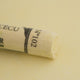A close-up of a yellow Sennelier extra soft pastel. on the same coloured background, with the colour information printed on the paper wrap.