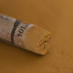 A close-up of a brown Sennelier extra soft pastel on the same coloured background, with the colour information printed on the paper wrap.