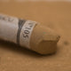 A close-up of a brown Sennelier extra soft pastel. on the same coloured background, with the colour information printed on the paper wrap.