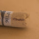 A close-up of a brown Sennelier extra soft pastel. on the same coloured background, with the colour information printed on the paper wrap.