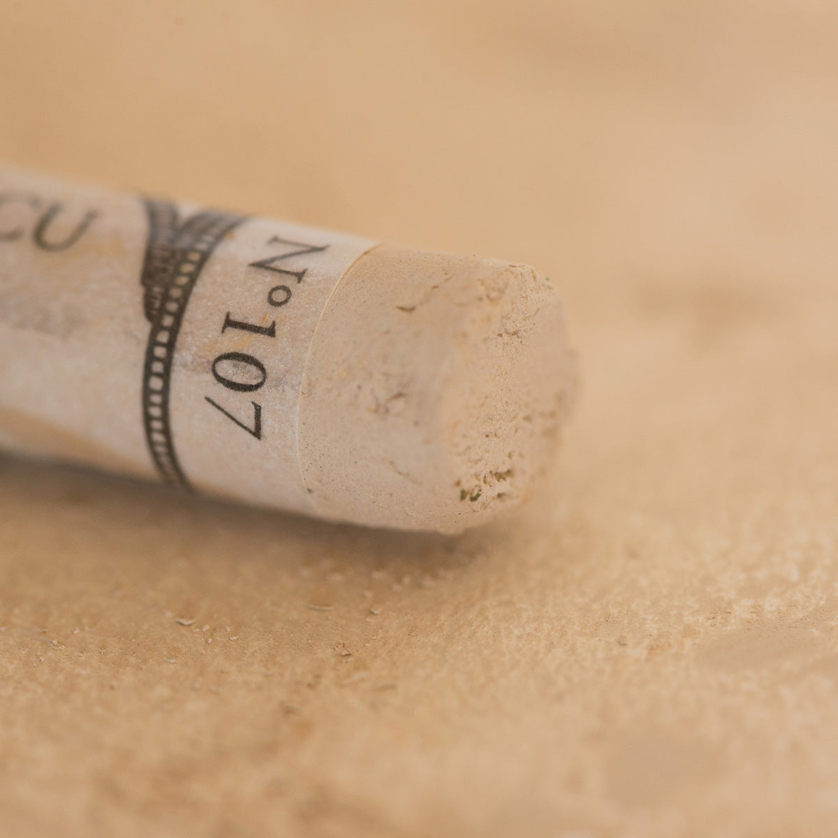 A close-up of a light brown Sennelier extra soft pastel. on the same coloured background, with the colour information printed on the paper wrap.