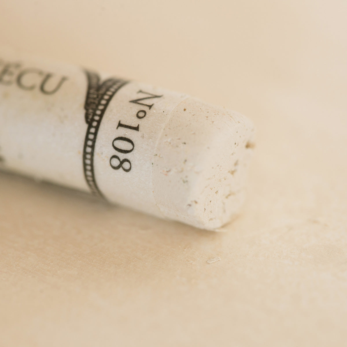 A close-up of a white Sennelier extra soft pastel. on the same coloured background, with the colour information printed on the paper wrap.