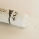 A close-up of a white Sennelier extra soft pastel. on the same coloured background, with the colour information printed on the paper wrap.