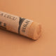 A close-up of a Sennelier extra soft pastel on a brown background with the colour information printed on the paper wrap.