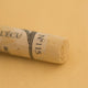 A close-up of a light yellow Sennelier extra soft pastel. on the same coloured background, with the colour information printed on the paper wrap.