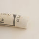 A close-up of a white Sennelier extra soft pastel. on the same coloured background, with the colour information printed on the paper wrap.