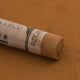 A close-up of a Sennelier extra soft pastel on a brown background with the colour information printed on the paper wrap.