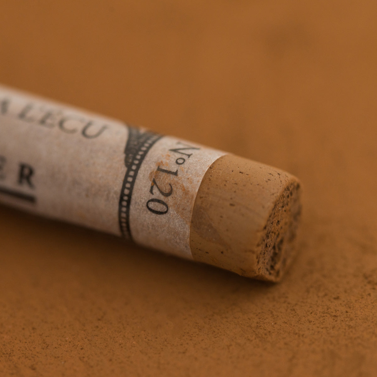 A close-up of a Sennelier extra soft pastel on a brown background with the colour information printed on the paper wrap.