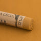 A close-up of a Sennelier extra soft pastel on a brown background with the colour information printed on the paper wrap.