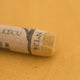 A close-up of a Sennelier extra soft pastel on a brown background with the colour information printed on the paper wrap.