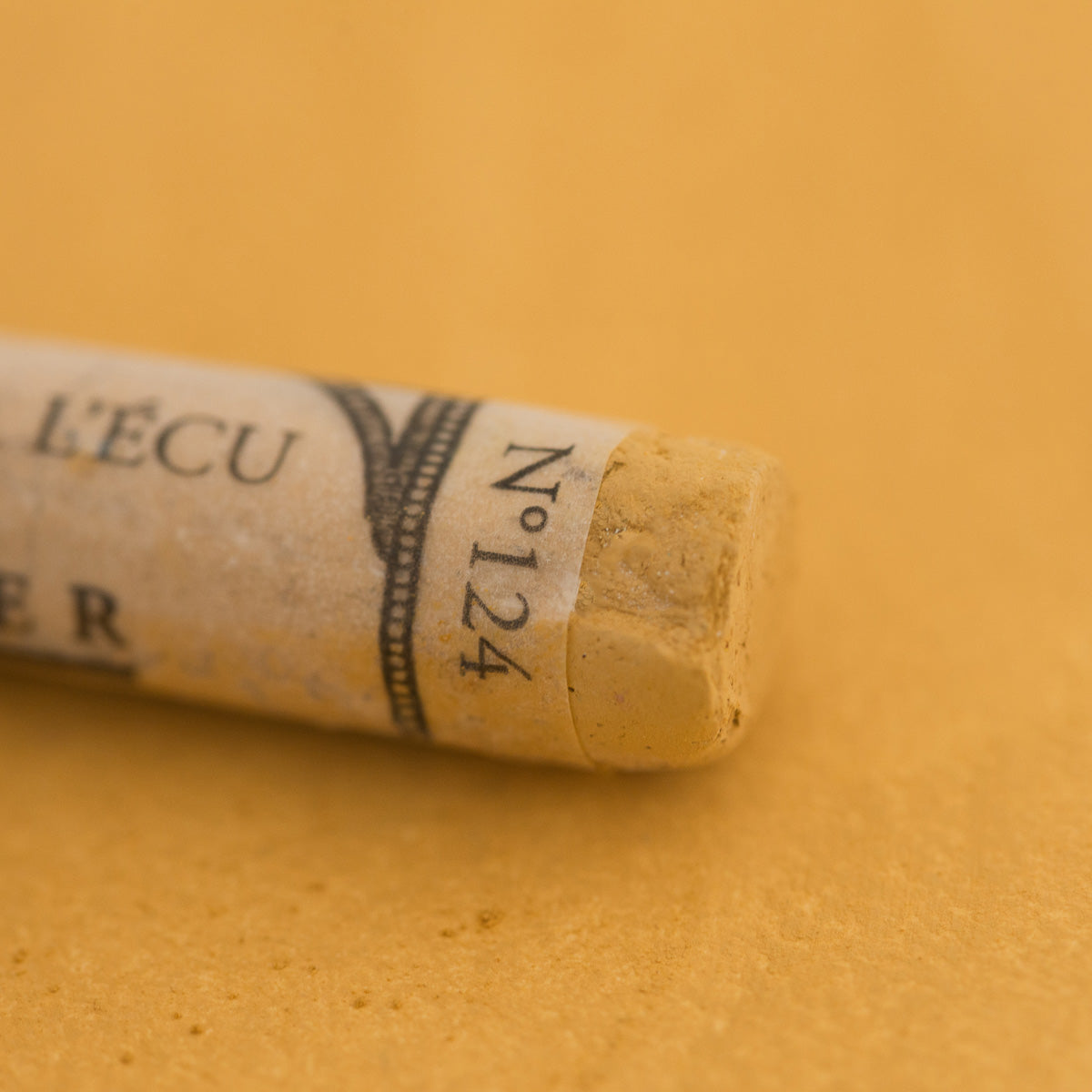 A close-up of a Sennelier extra soft pastel on a brown background with the colour information printed on the paper wrap.