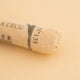 A close-up of a pale orange Sennelier extra soft pastel. on the same coloured background, with the colour information printed on the paper wrap.