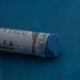A close-up of a blue Sennelier extra soft pastel on the same coloured background, with the colour information printed on the paper wrap.