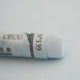 A close-up of a white Sennelier extra soft pastel on the same coloured background, with the colour information printed on the paper wrap.