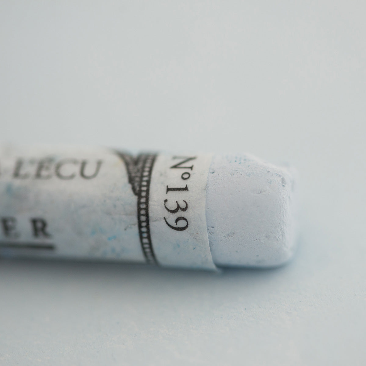 A close-up of a white Sennelier extra soft pastel on the same coloured background, with the colour information printed on the paper wrap.