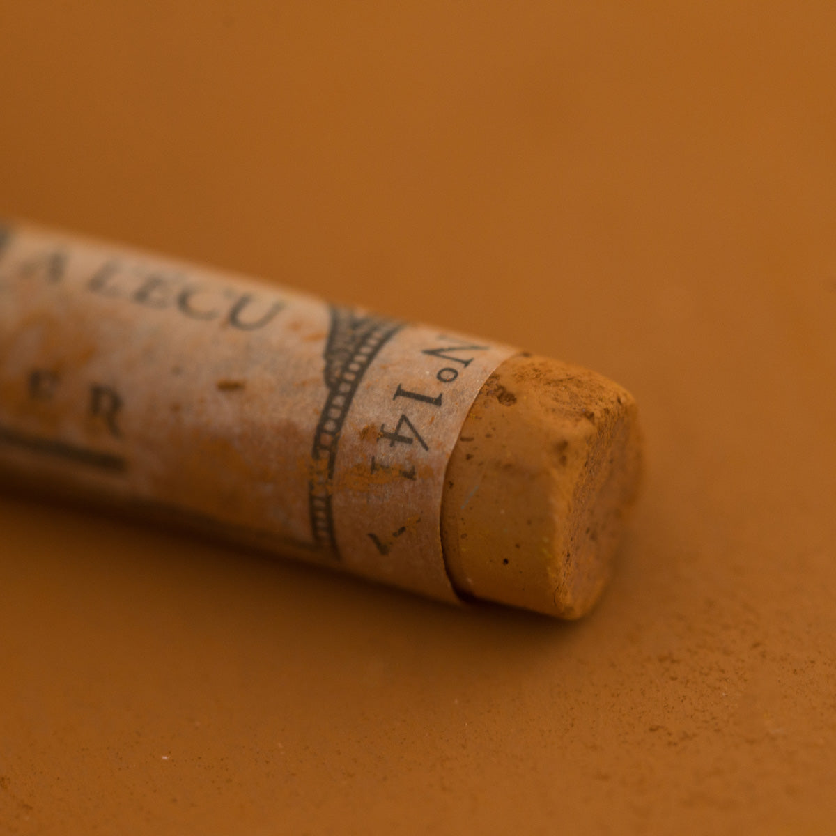 A close-up of a Sennelier extra soft pastel on a brown background with the colour information printed on the paper wrap.
