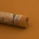 A close-up of a Sennelier extra soft pastel on a brown background with the colour information printed on the paper wrap.