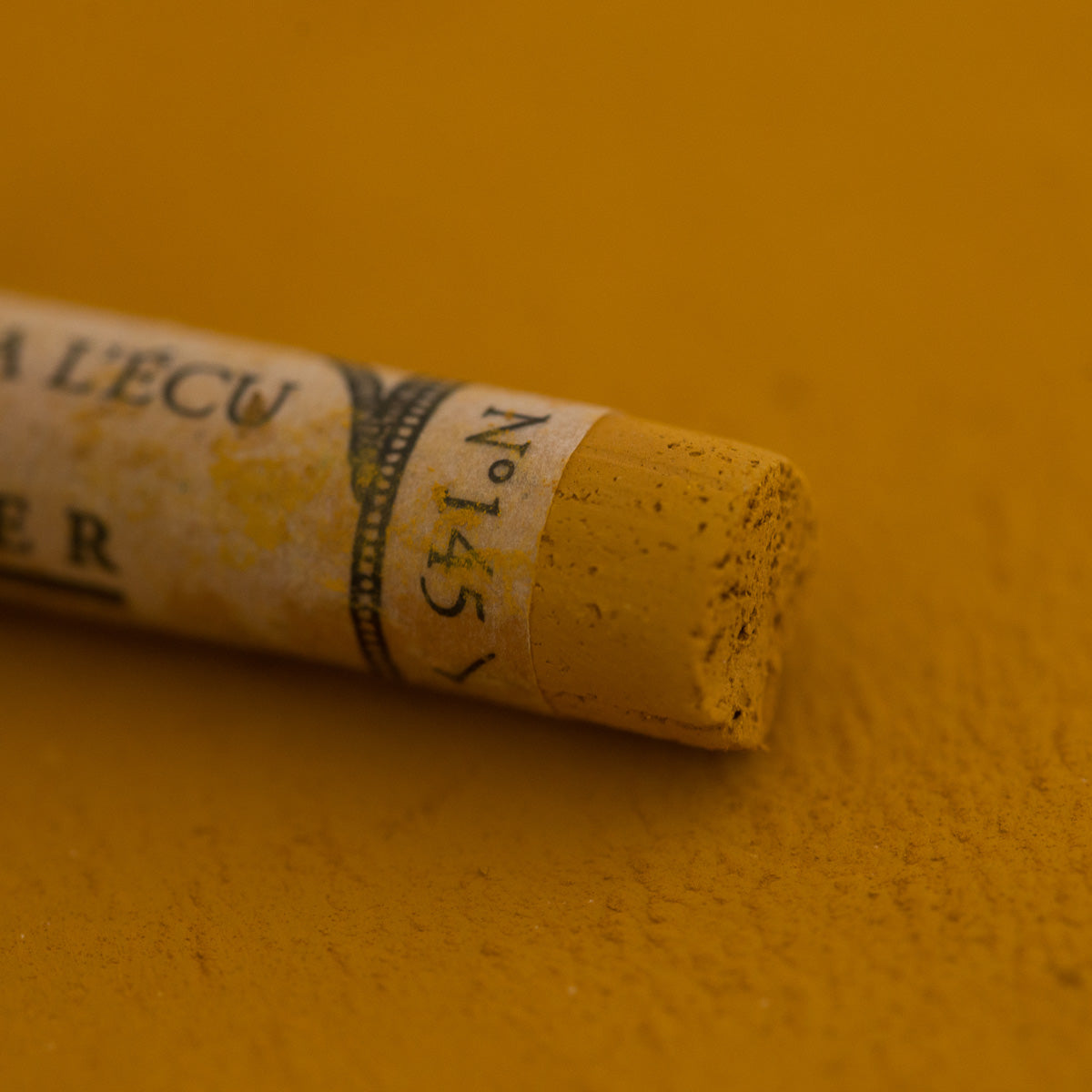 A close-up of a Sennelier extra soft pastel on a green brown background with the colour information printed on the paper wrap.