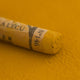 A close-up of a Sennelier extra soft pastel on a green brown background with the colour information printed on the paper wrap.
