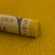 A close-up of a Sennelier extra soft pastel on a green background with the colour information printed on the paper wrap.