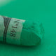 A close-up of a green Sennelier extra soft pastel. on the same coloured background, with the colour information printed on the paper wrap.