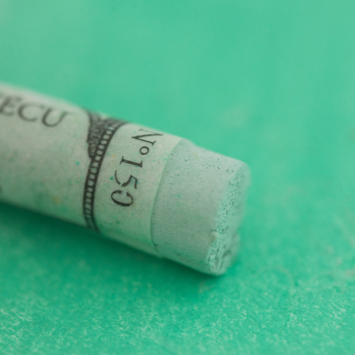 A close-up of a green Sennelier extra soft pastel. on the same coloured background, with the colour information printed on the paper wrap.