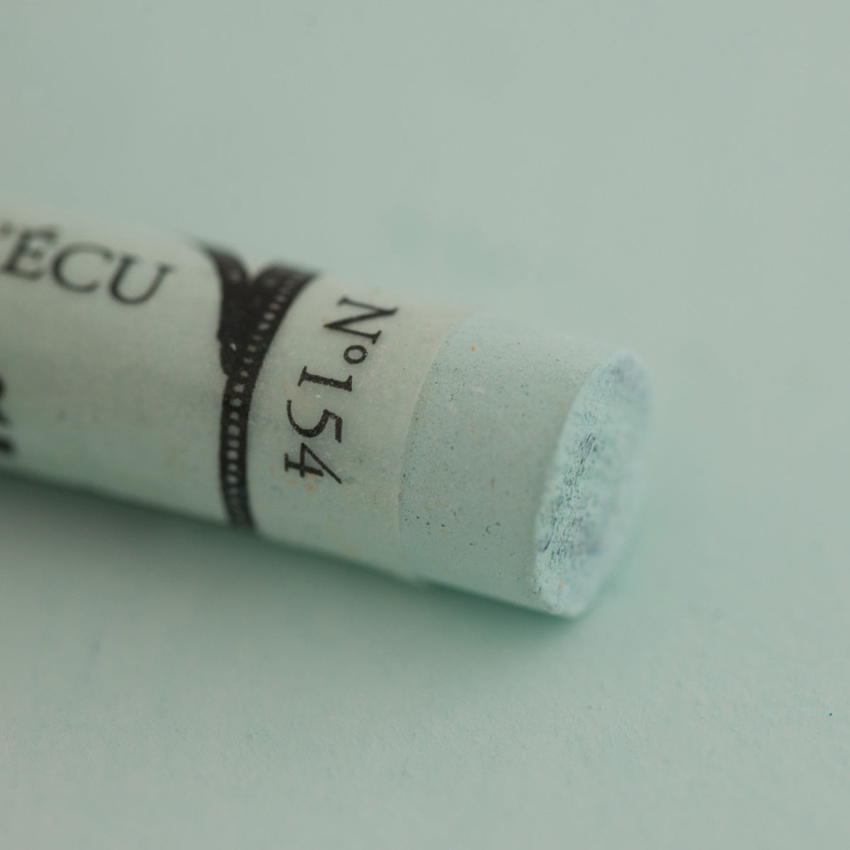 A close-up of a white green Sennelier extra soft pastel. on the same coloured background, with the colour information printed on the paper wrap.