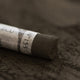 A close-up of a brown Sennelier extra soft pastel, on the same coloured background, with the colour information printed on the paper wrap.
