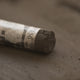 A close-up of a brown Sennelier extra soft pastel, on the same coloured background, with the colour information printed on the paper wrap.
