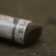 A close-up of a brown Sennelier extra soft pastel, on the same coloured background, with the colour information printed on the paper wrap.