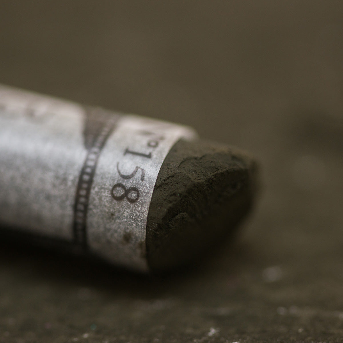 A close-up of a brown Sennelier extra soft pastel, on the same coloured background, with the colour information printed on the paper wrap.
