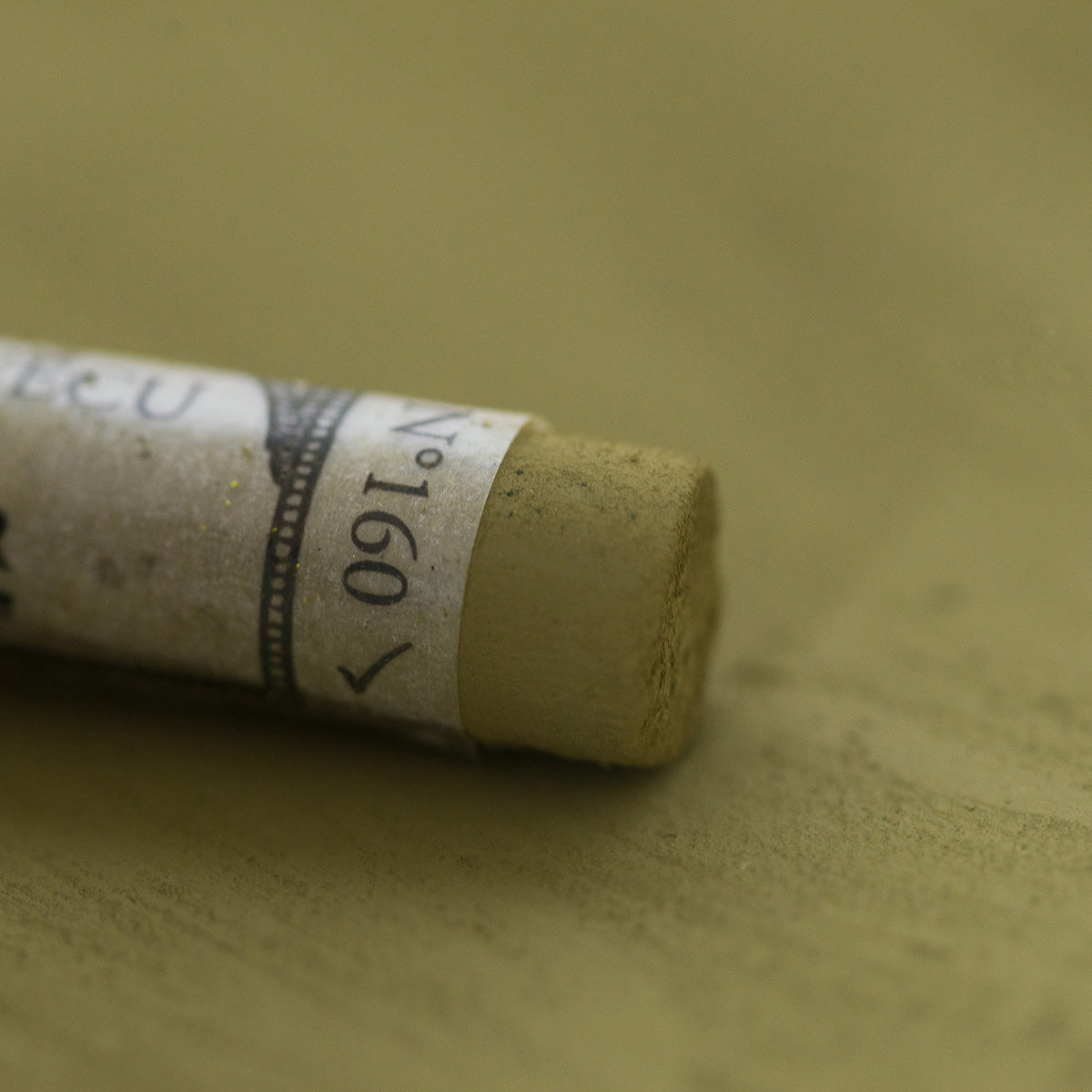 A close-up of a green Sennelier extra soft pastel, on the same coloured background, with the colour information printed on the paper wrap.