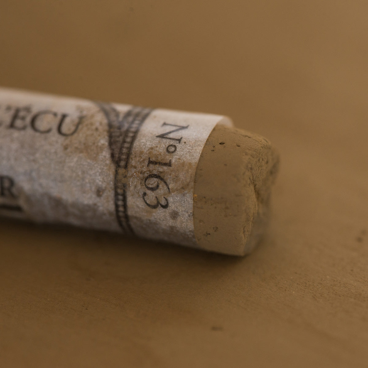 A close-up of a brown Sennelier extra soft pastel. on the same coloured background, with the colour information printed on the paper wrap.