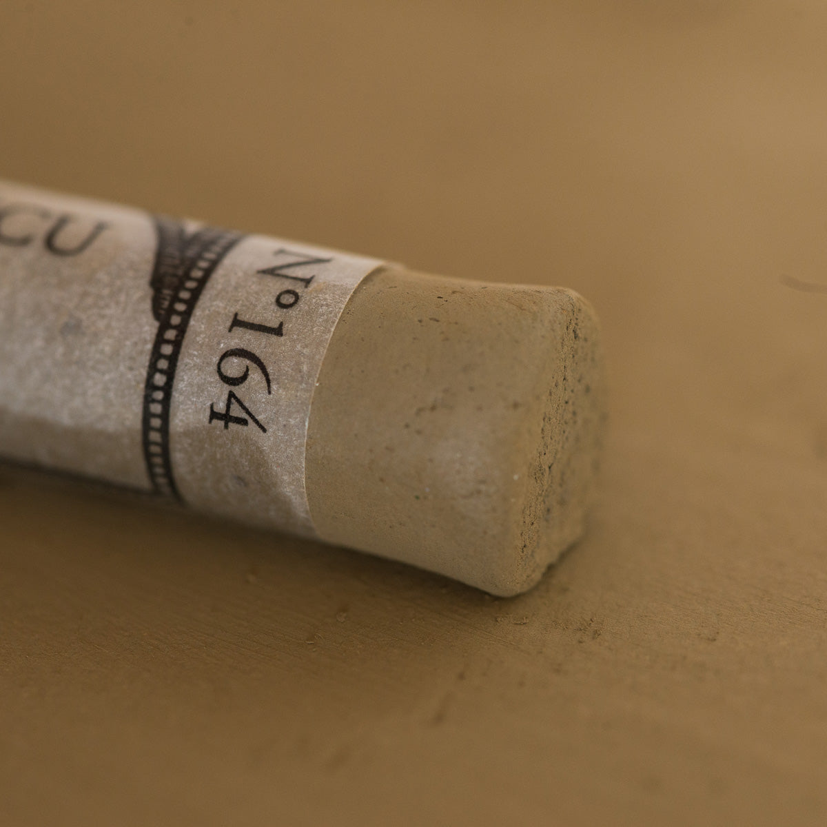 A close-up of a Sennelier extra soft pastel. on the same coloured background, with the colour information printed on the paper wrap.