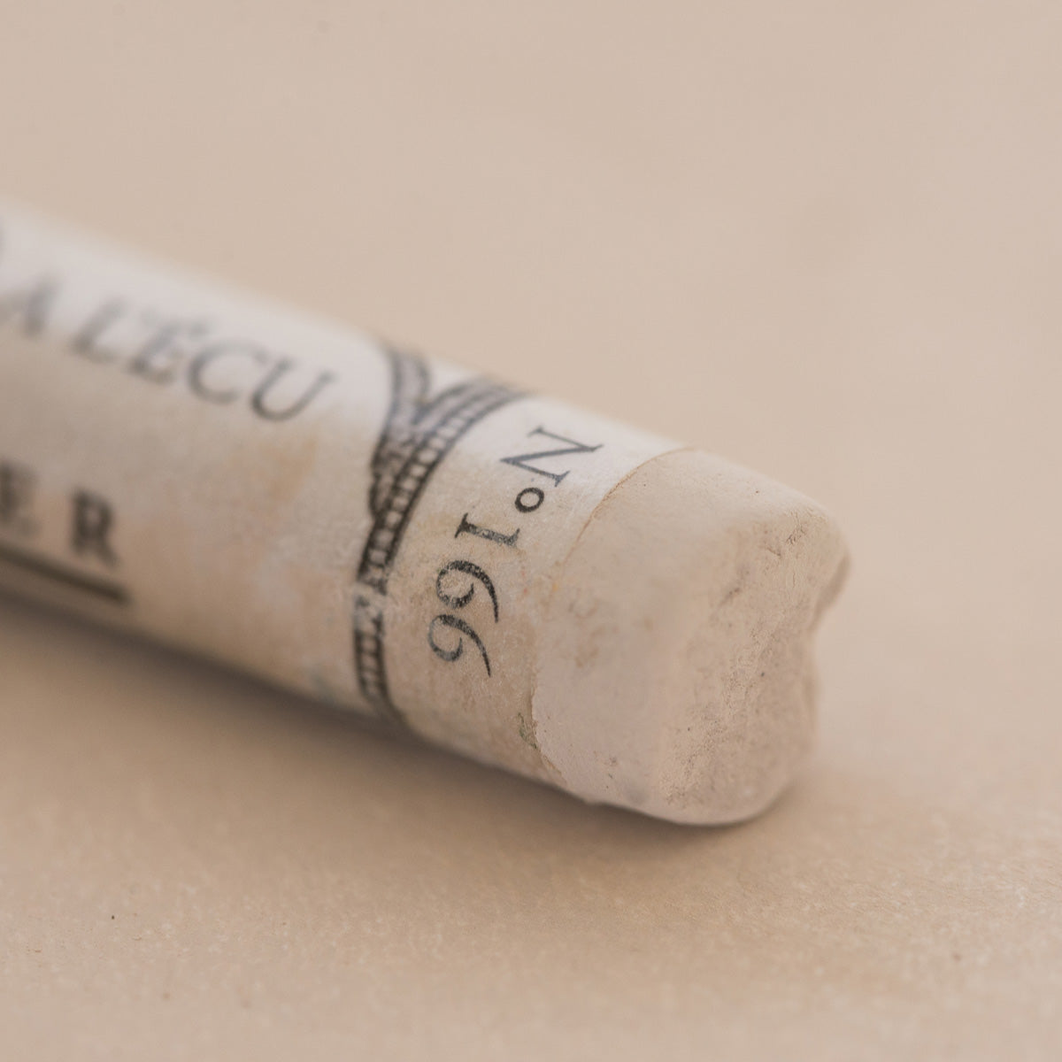 A close-up of a white Sennelier extra soft pastel. on the same coloured background, with the colour information printed on the paper wrap.