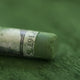 A close-up of a green Sennelier extra soft pastel. on the same coloured background, with the colour information printed on the paper wrap.