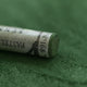 A close-up of a green Sennelier extra soft pastel. on the same coloured background, with the colour information printed on the paper wrap.