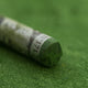 A close-up of a green Sennelier extra soft pastel. on the same coloured background, with the colour information printed on the paper wrap.