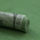 A close-up of a green Sennelier extra soft pastel. on the same coloured background, with the colour information printed on the paper wrap.