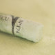 A close-up of a white Sennelier extra soft pastel. on the same coloured background, with the colour information printed on the paper wrap.