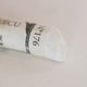 A close-up of a white Sennelier extra soft pastel. on the same coloured background, with the colour information printed on the paper wrap.