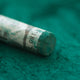 A close-up of a green Sennelier extra soft pastel, on the same coloured background, with the colour information printed on the paper wrap.