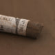 A close-up of a brown Sennelier extra soft pastel with the colour information printed on the paper wrap.
